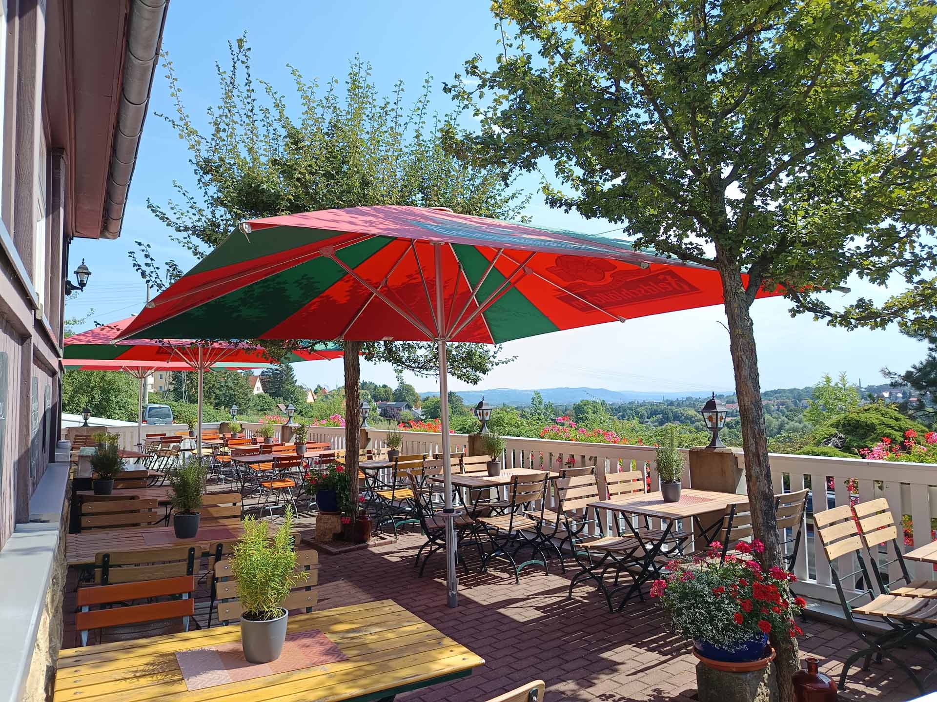 Leere Terrasse mit roten Sonnenschirmen und grünen Akzenten sowie Blumen