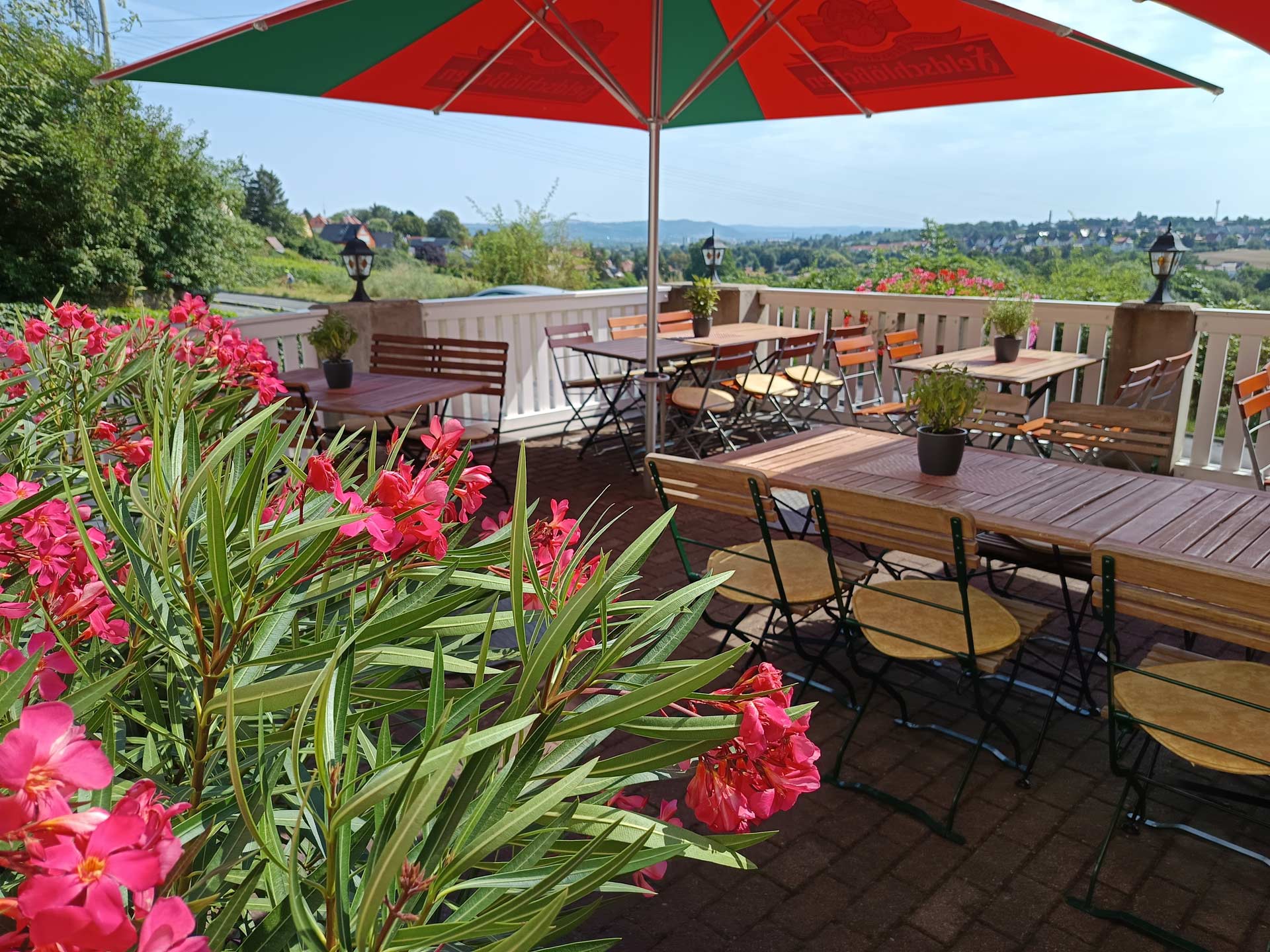 Leere Terrasse mit roten Blumen und rot gruenem Sonnenschirm, heiter