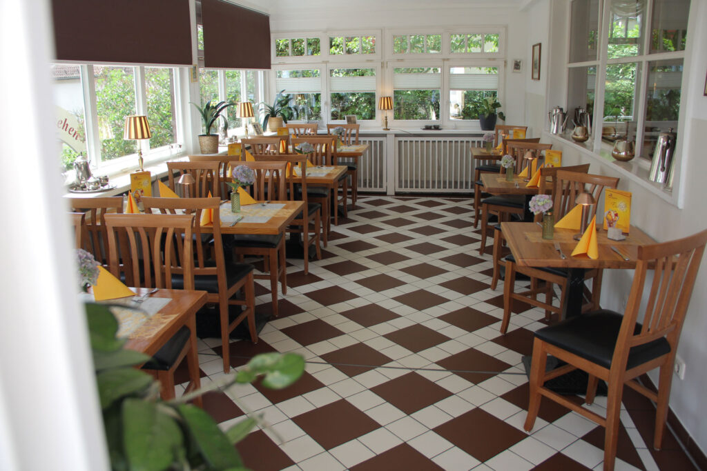 Leeres Cafe mit braunen Holztischen und Stuehlen sowie Schachbrettfliesen