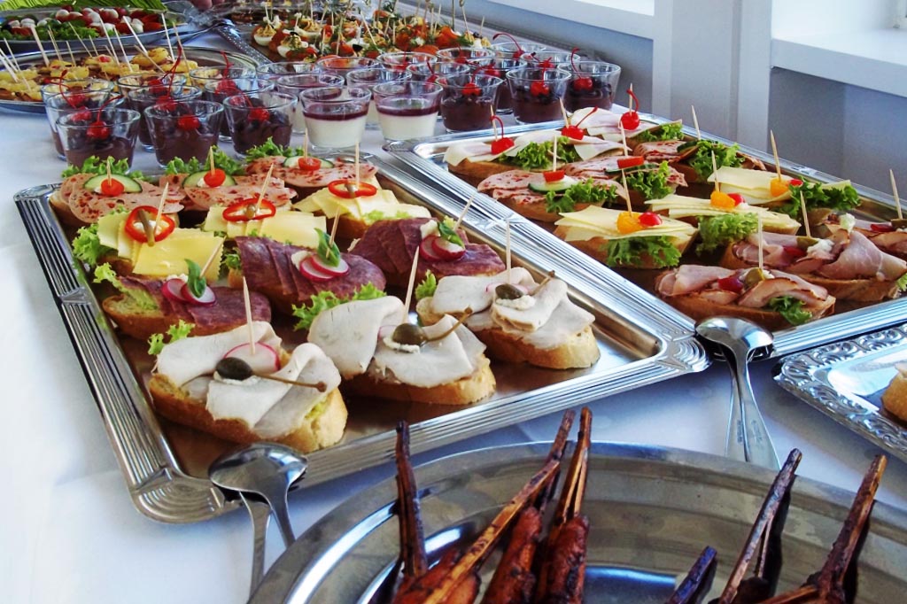 Buntes Buffet mit belegten Broten und Dessertgläsern auf Silberplatten