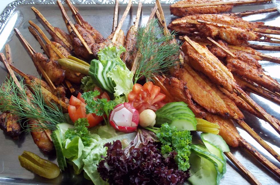 Gegrillte Fleischspieße und braune Kartoffelspalten mit buntem Salatgarnitur