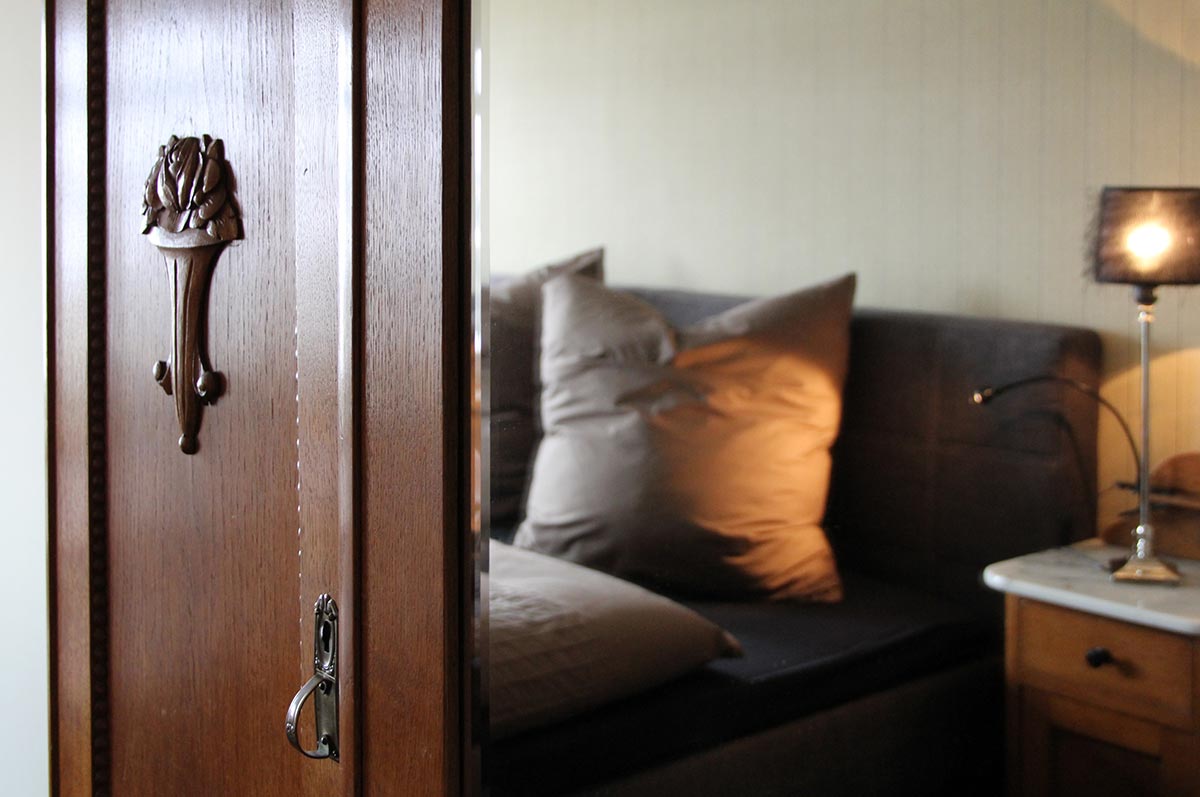 Braunes  Holzmoebel  neben  Sofa  mit  grauen  Kissen  und  warmer  Lampe