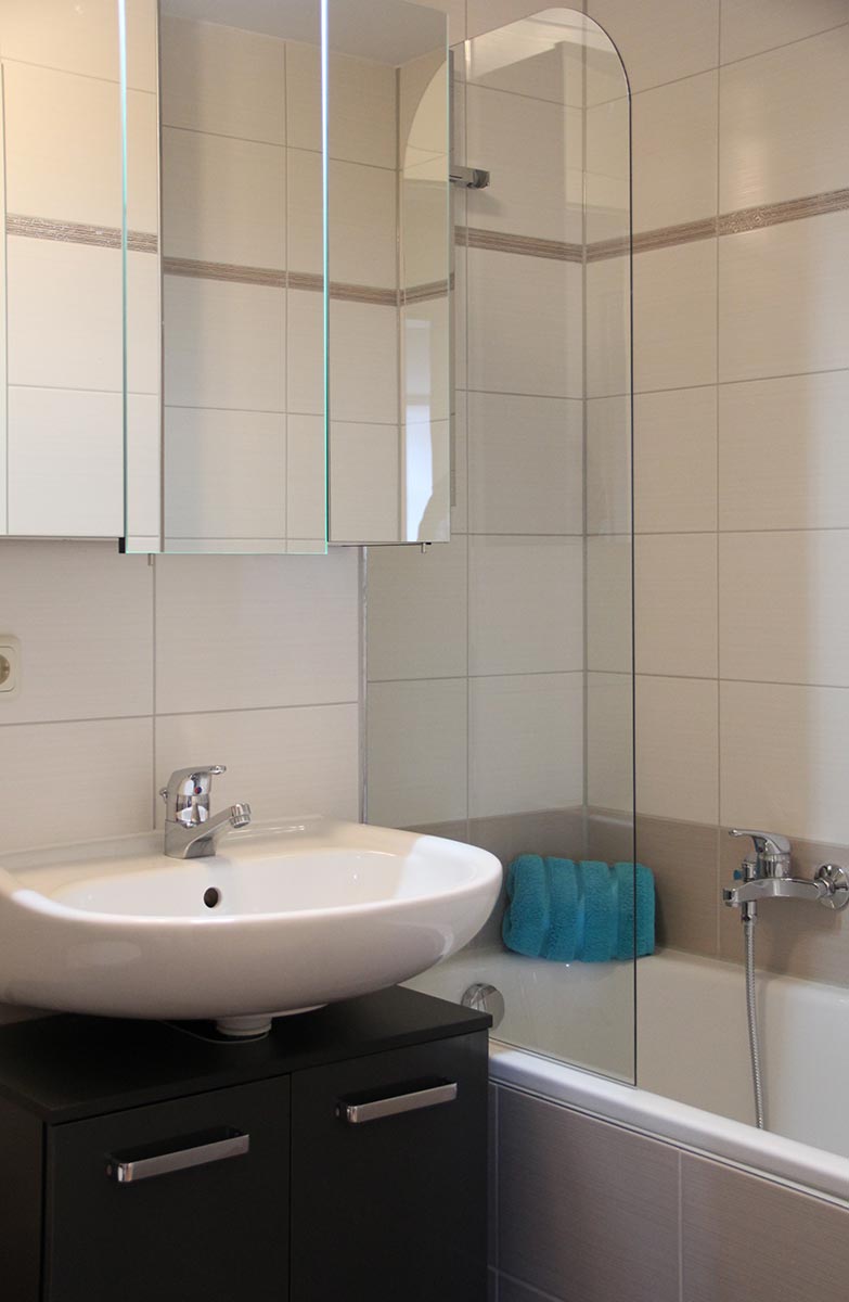 Beiges  Bad  mit  Waschtisch,  Glasduschwand,  Wanne  und  blauem  Handtuch
