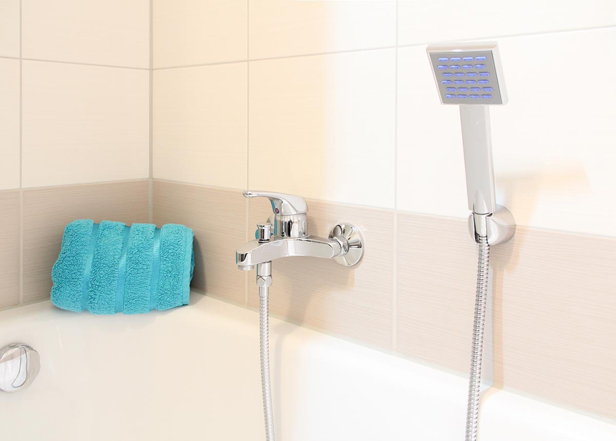 Hellblaues  Handtuch  an  weisser  Badewanne  neben  Chromarmatur  und  Duschkopf