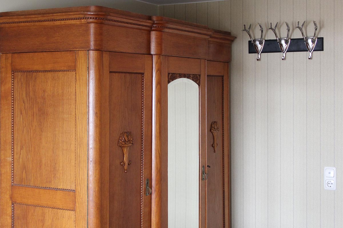 Brauner Holzschrank mit Spiegel, daneben silberne Hakenleiste an Wand