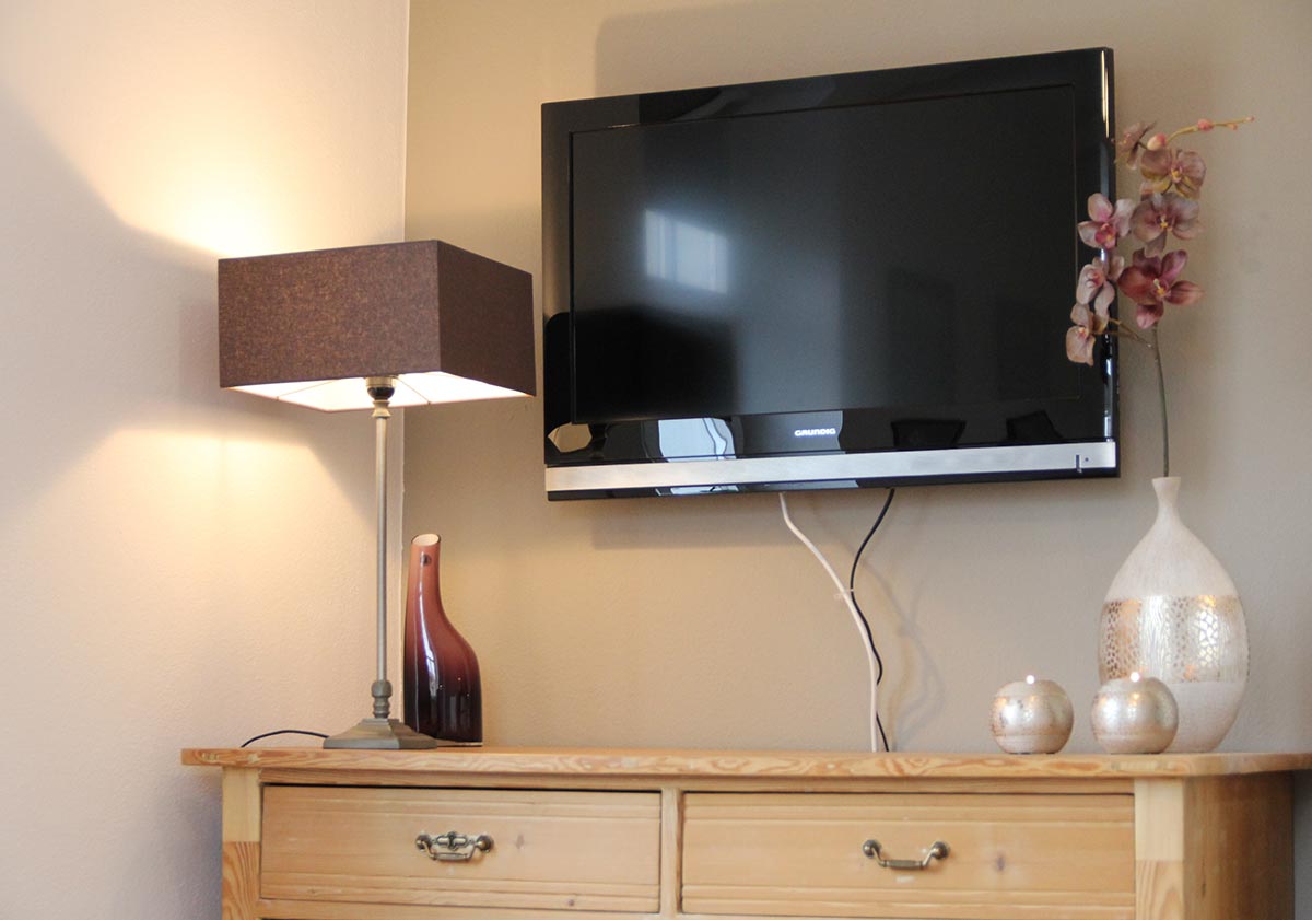 Schwarzer  Fernseher  ueber  Holzkommode  mit  Lampe  und  Vasen  in  Beige