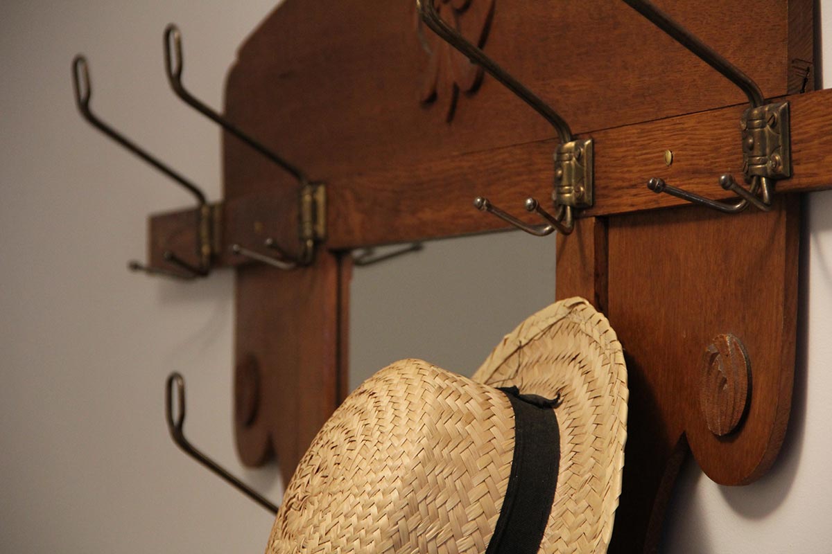 Strohhut  mit  schwarzem  Band  an  brauner  Holzgarderobe  mit  Haken