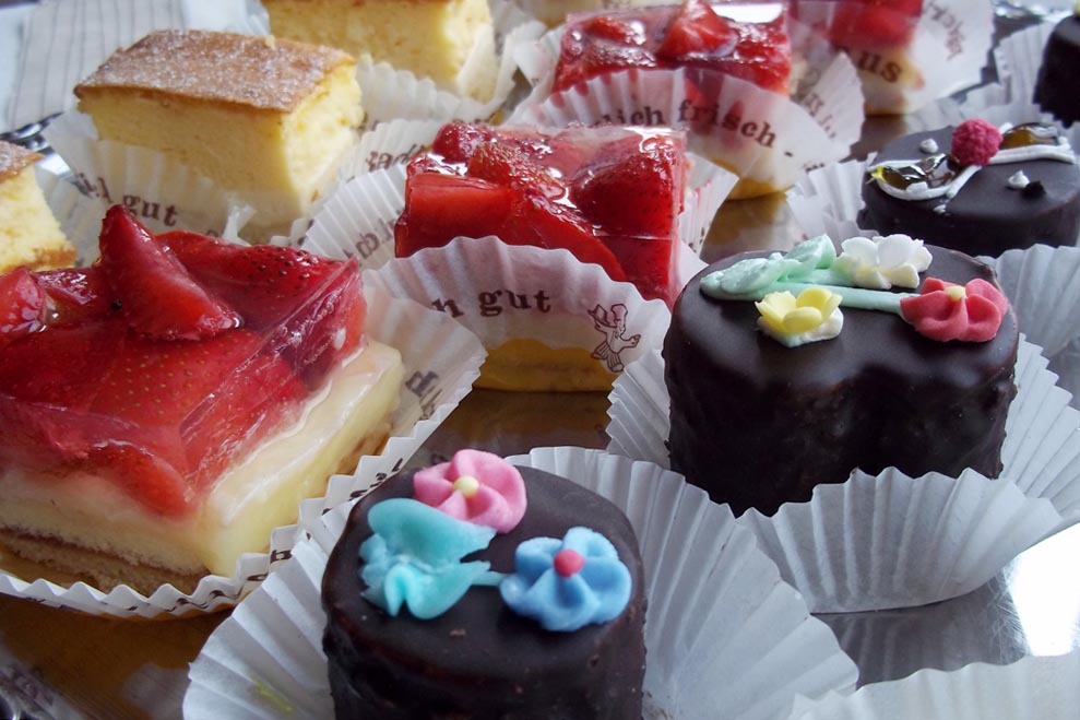 Bunte Petit Fours mit Erdbeerglasur und Schokoguss sowie Blumenverzierung