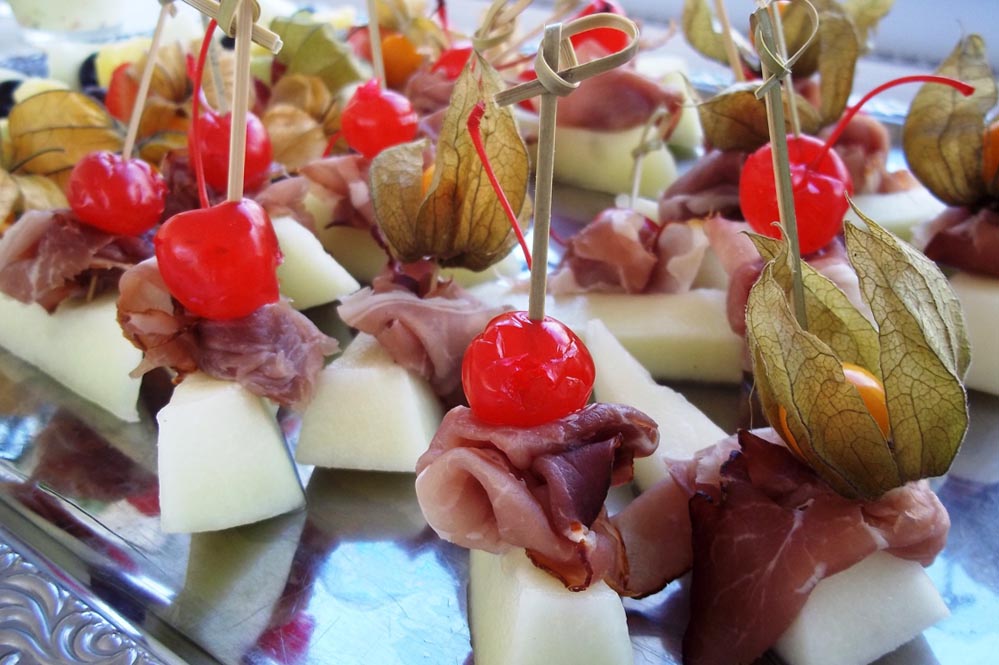Appetithappen mit rohem Schinken, Melone, Kirsche und Physalis, farbig