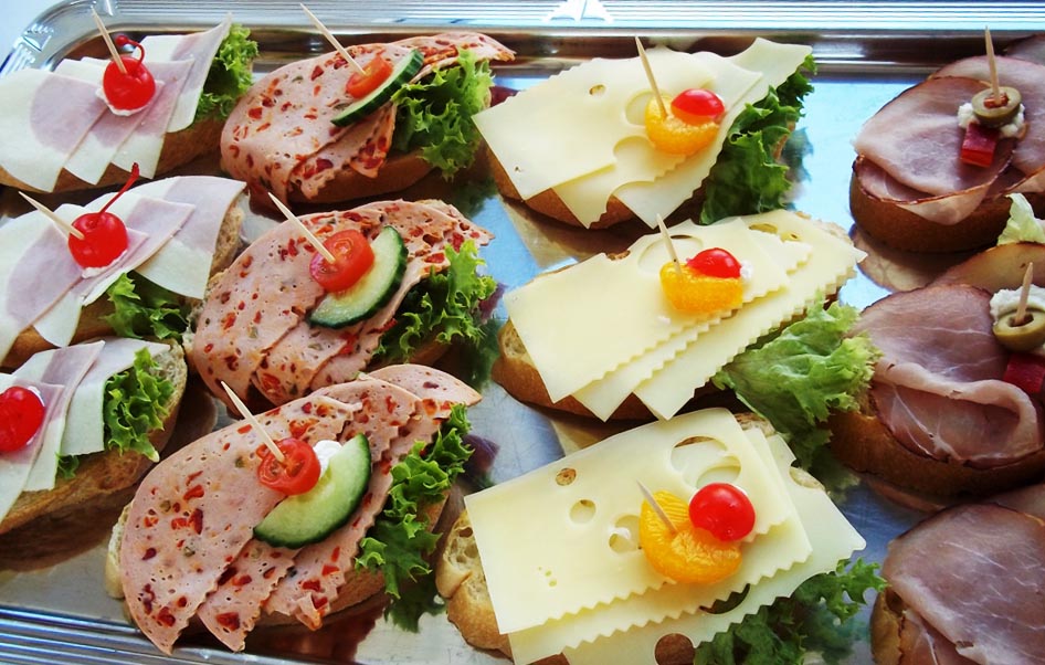 Aufschnitt und Kaesebrote in Hellbraun mit bunten Kirschen und Salatbeilage