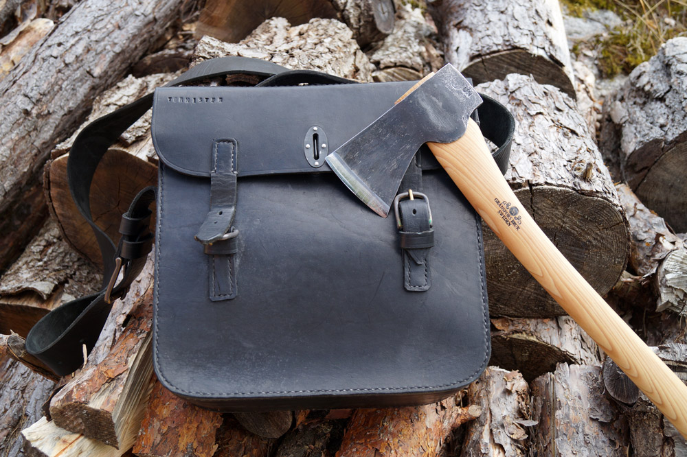 Schwarze Ledertasche und Axt, robust, auf hellen Holzstapeln liegend