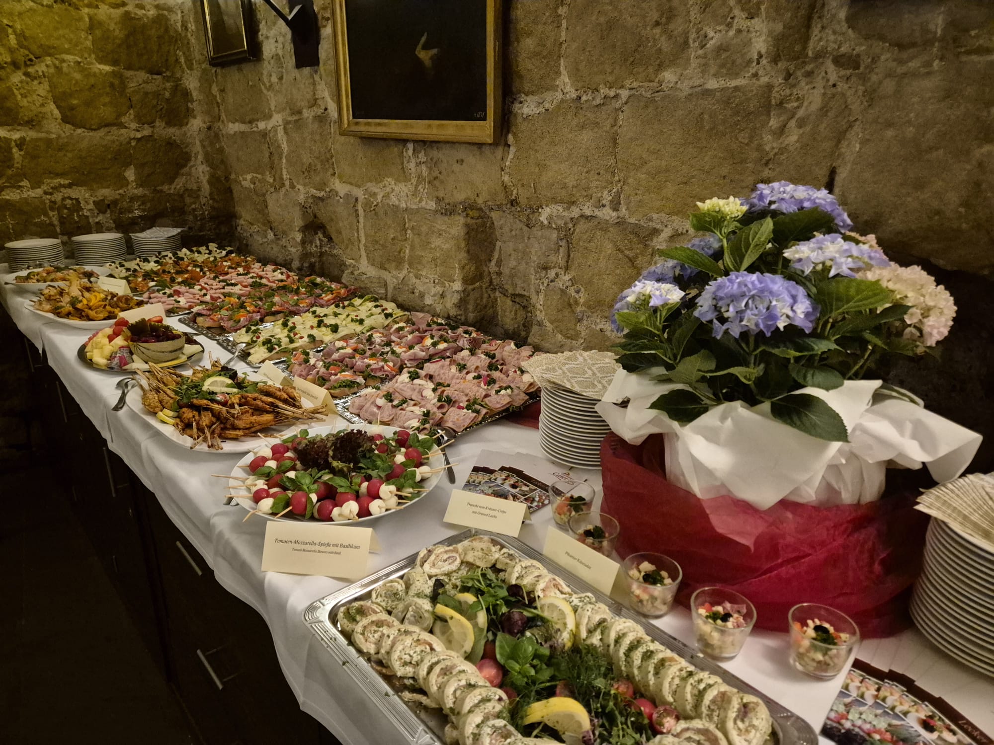 Buffet mit farbigen Häppchen, frischen Blumen und rustikaler Steinwand