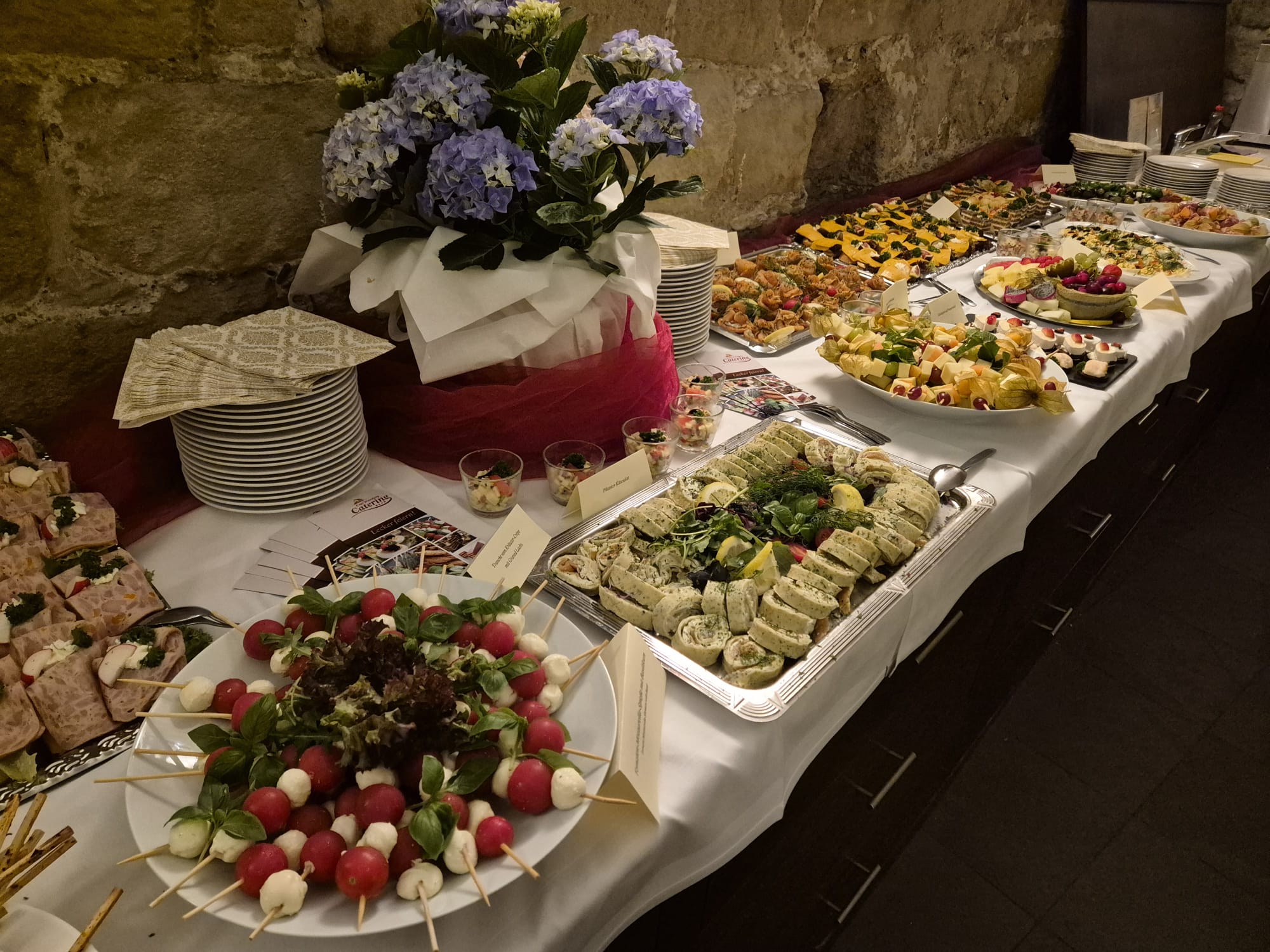 Buntes Buffet mit Häppchen und Salat, lila Blumen als Blickfang